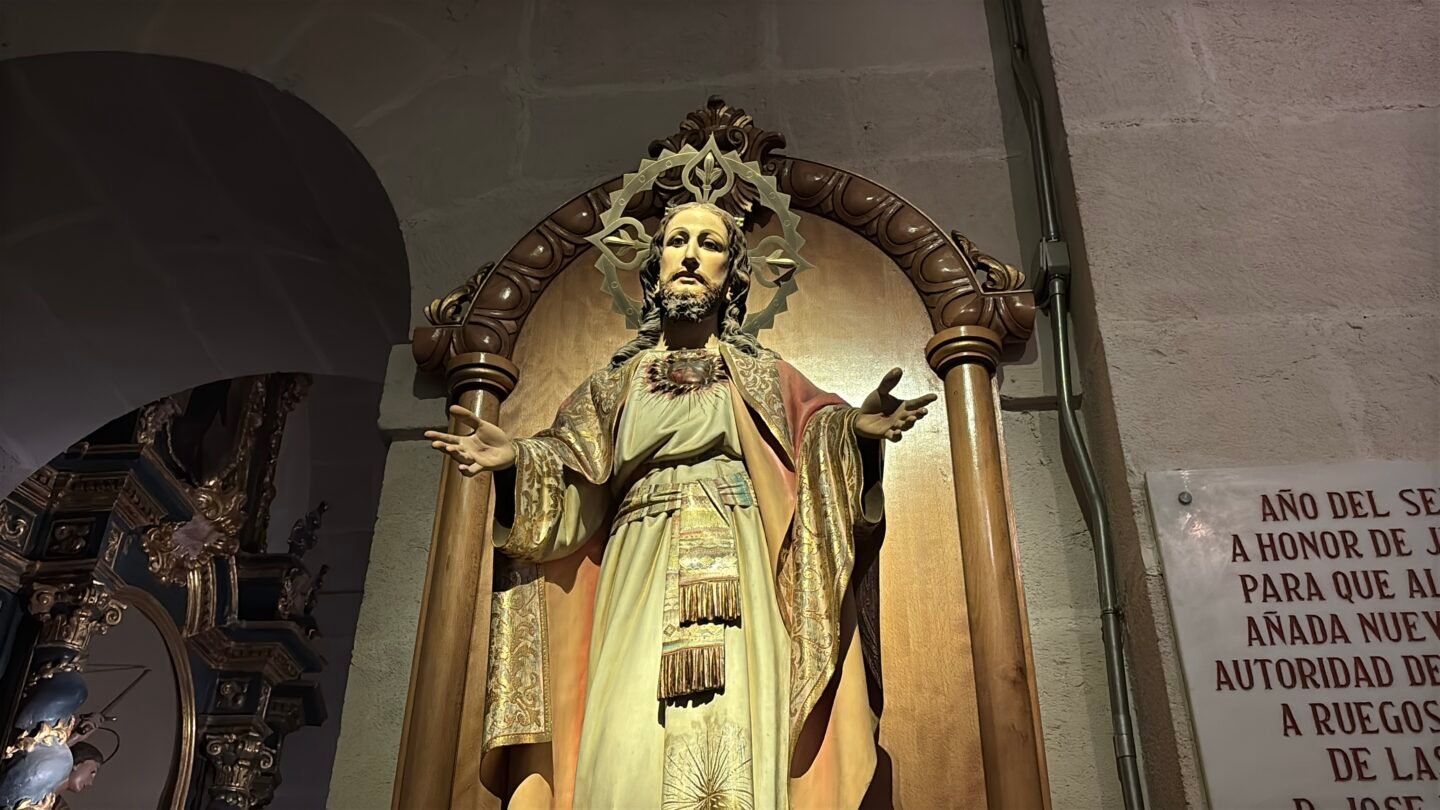Escultura religiosa del Sagrado Coraz&oacute;n de Jes&uacute;s con los brazos abiertos dentro de un marco de madera en el interior de la Concatedral de San Nicol&aacute;s de Bari en Alicante. La imagen viste t&uacute;nica clara y manto dorado, destacando detalles de arte sacro barroco.